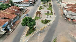 the scene unfolds throughout the entire plaza area. The car drives down the road. The tree's foliage moves slightly in the wind. in a cinematic scene with professional lighting, shallow depth of field, and movie-quality visual effects