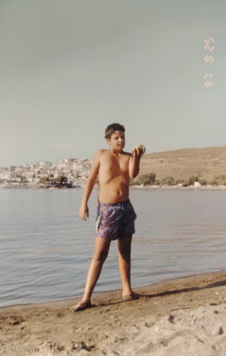 Create a short, highly realistic video of a 10-year-old child standing on the seashore, holding and showing a seashell to the camera. Preserve natural proportions, facial features, and a consistent, realistic expression — calm, slightly curious or proud, but not exaggerated. No overacting, no artificial smiles or dramatic gestures.

Maintain full realism: no stylization, no beautification, no artificial smoothing.

The child should make small, natural movements only: gently raising the shell, slight hand adjustments, minimal head movement, and subtle breathing. Movements must feel spontaneous and physically accurate, never staged or exaggerated.

Animate the environment with soft, natural motion: gentle ocean waves rolling in the background, subtle water movement, and a light sea breeze causing slight movement in hair and clothing. The shoreline should remain stable, with no sudden or strong environmental changes.

Lighting should reflect natural daylight at the beach: soft, balanced highlights, realistic skin tones, and accurate colors — not oversaturated.

Motion must be smooth and cinematic: no abrupt transitions, no jitter, no distortion, no morphing artifacts. Camera should remain stable, as if handheld but steady, or fixed in place.

Overall feeling: authentic, calm, and natural — like a real candid moment of a child quietly showing a small discovery.