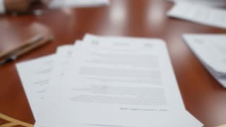 Photorealistic 4K cinematic video. The scene starts with a tight zoom-in on an executive office desk with documents neatly placed on top. Slow, smooth camera movement. The camera then gradually pulls back, revealing a large wooden meeting table with four Saudi men wearing traditional white thobes and ghutra, seated around the table reviewing documents.

The camera continues pulling back and then transitions into a slow vertical crane shot, rising upward to reveal the full meeting room from above. Symmetrical composition, polished wooden interior, green leather chairs, and official portraits on the wall behind the main desk.

Natural indoor lighting, soft shadows, realistic reflections on the table surface. Calm, professional atmosphere. Subtle hand movements as they review papers. No direct eye contact with camera.

No text, no dialogue, no music. Only natural ambient room sound. Cinematic, ultra-detailed, smooth transitions