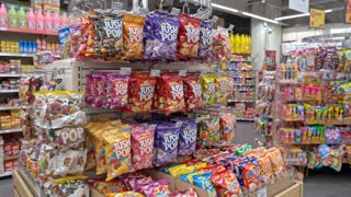 Animate this image with a very subtle, realistic cinematic camera movement. Apply a slow, smooth forward dolly-in with a gentle sideways camera drift, creating natural depth and parallax between the foreground candy shelves and the background. Keep the movement minimal, steady, and physically realistic, as if filmed by a professional camera operator inside a real supermarket. Preserve all original product packaging, colors, text, shelf positions, lighting, and proportions exactly as they are. No object movement, no floating products, no morphing, no flickering, no warping, no artificial zoom, and no sudden camera movements. Maintain realistic indoor lighting and natural reflections. One continuous shot, approximately 5–7 seconds, photorealistic, stable, and seamless.