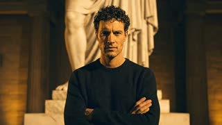 Cinematic founder video. A man with curly dark hair, arms crossed, standing in a dimly lit classical museum at night with a large ancient Greek marble statue behind him. He looks directly into the camera with a calm, intense gaze and says: "I got tired of overpriced jewelry that tarnishes in a week and means nothing." Warm golden light from below, dramatic shadows, marble textures visible in background. Slow push-in camera movement. Cinematic 24fps. No text overlay. Realistic lip sync. Low, confident, slightly tired male voice.
