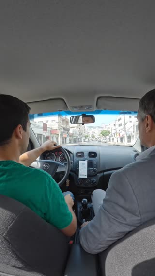 Scene 3: Now, with the camera positioned at a different angle, it films the two characters in the same place. The driver continues driving the vehicle and puts his hand to his head, appearing worried and distressed. The passenger, observing the driver's concern, asks a question in Brazilian Portuguese in a calm voice: "Are you alright, my friend?"